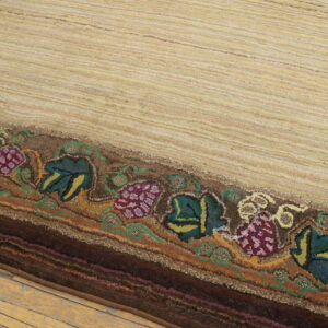 Textured beige striped rug with a thick border featuring deep purple grape and green leaf designs on wooden flooring.