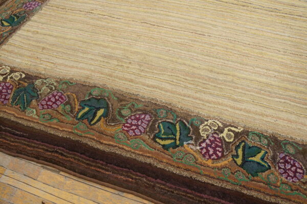 Textured beige striped rug with a thick border featuring deep purple grape and green leaf designs on wooden flooring.