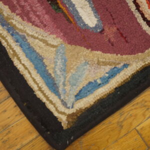 Textured corner of a magenta, cream, and blue patterned rug resting on yellow wooden planks.