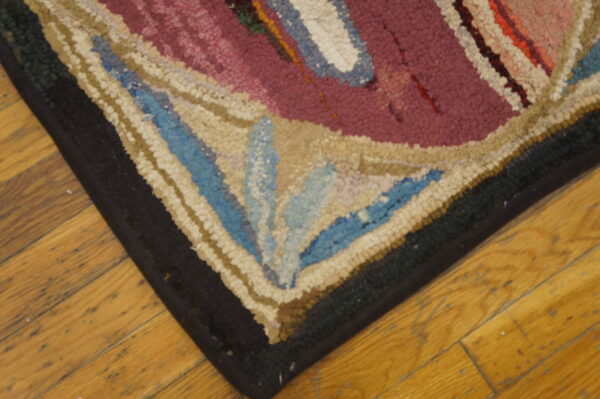 Textured corner of a magenta, cream, and blue patterned rug resting on yellow wooden planks.