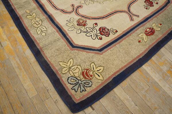 Close-up of a floral rug corner with red roses, blue accents, and a textured taupe border on worn wood.