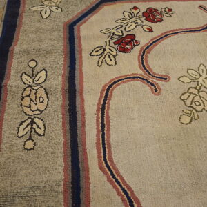 Textured floral rug in beige, gray, red, and blue resting on yellow-toned plank flooring.