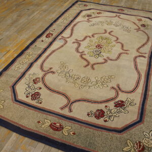 Traditional beige floral rug featuring a navy and red border on distressed wooden floors.