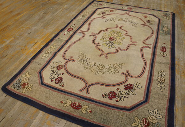 Traditional beige floral rug featuring a navy and red border on distressed wooden floors.