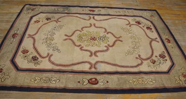 Floral rug featuring a cream field, red roses, and a gray-green border sits on wood planks.
