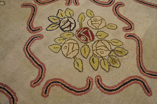 Textured beige rug with a floral pattern of red and pale roses, framed by wavy black, rust, and gold borders.