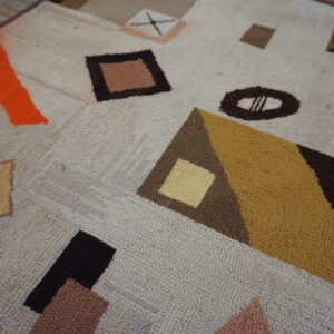 Chunky loop pile rug featuring abstract orange, mustard, and brown geometric shapes on wooden flooring.