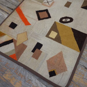 Textured cream rug with brown, orange, and mustard abstract shapes resting on weathered gray floorboards.