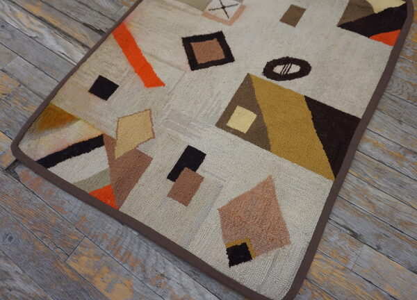 Textured cream rug with brown, orange, and mustard abstract shapes resting on weathered gray floorboards.