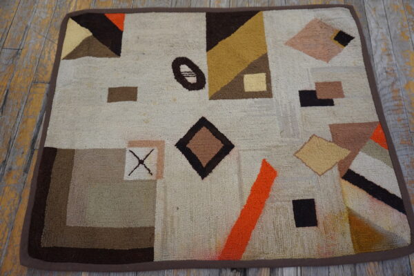A small, looped rug displays geometric shapes in cream, brown, orange, and gold on wooden flooring.