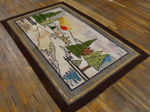 A rectangular rug featuring a detailed mountain landscape scene with green trees and a thick dark brown border.