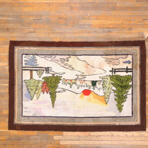 Multicolor hooked rug with a folk art landscape scene and thick brown border on hardwood floor planks.