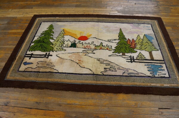 Hooked rug with a woodland scene and sunset pattern, framed by a dark border on worn wood planks.