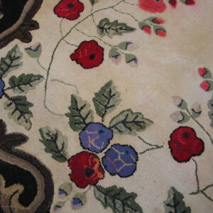 Close-up of a textured loop pile rug showing red, blue, and green florals against cream with a dark scrolled border.
