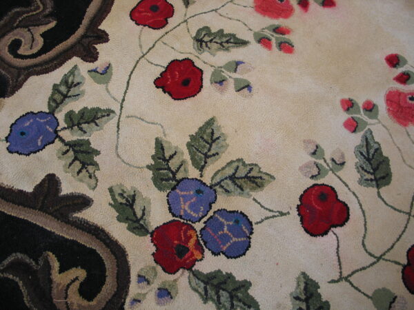 Close-up of a textured loop pile rug showing red, blue, and green florals against cream with a dark scrolled border.