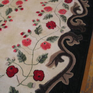 Floral cream rug with red blooms and a dark sculpted border rests on light brown wood flooring.