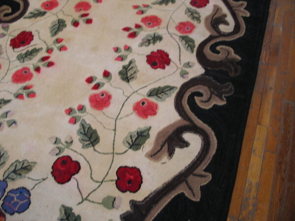 Floral cream rug with red blooms and a dark sculpted border rests on light brown wood flooring.