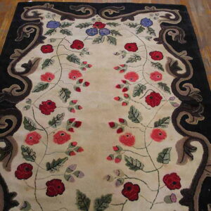 High-pile rug featuring red and blue florals on a cream ground with a black scrolled border on wood.