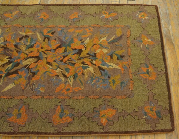 Textured brown and olive green rug with a dense orange, blue, and gold floral pattern on a wood floor.