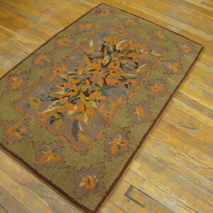 High-pile rug with a central orange and blue floral design and moss green border on distressed wood planks.