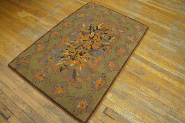 High-pile rug with a central orange and blue floral design and moss green border on distressed wood planks.