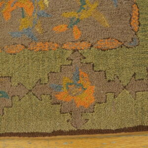 A textured hooked rug displays abstract floral patterns in brown, olive, orange, and blue resting on wood.