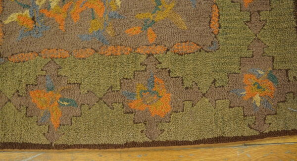 A textured hooked rug displays abstract floral patterns in brown, olive, orange, and blue resting on wood.