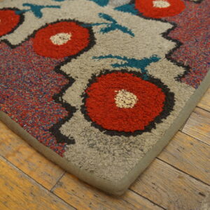 Textured rug with large red floral motifs and teal accents on a beige background, resting on rustic wood flooring.