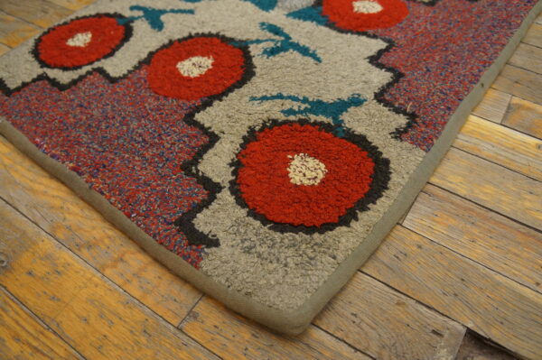 Textured rug with large red floral motifs and teal accents on a beige background, resting on rustic wood flooring.