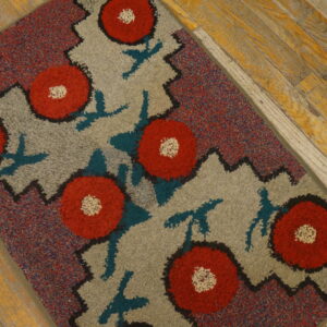 A loop pile rug featuring red flowers on gray, bordered by multicolor flecks, rests on wood planks.