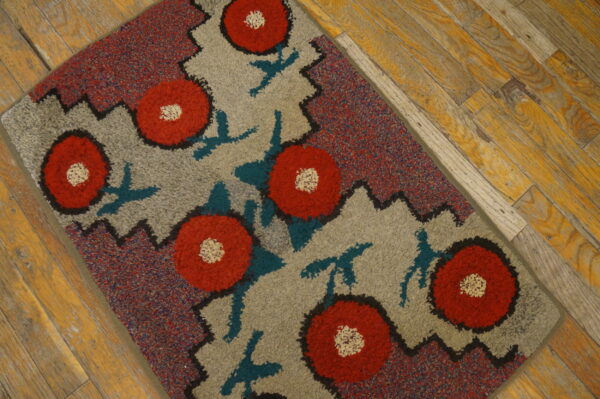 A loop pile rug featuring red flowers on gray, bordered by multicolor flecks, rests on wood planks.
