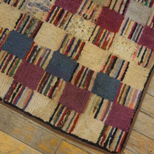 Close-up of a high-pile rug with a checkered pattern of beige, purple, blue, and multicolored striped blocks on wood flooring.
