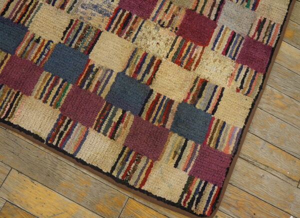 Close-up of a high-pile rug with a checkered pattern of beige, purple, blue, and multicolored striped blocks on wood flooring.