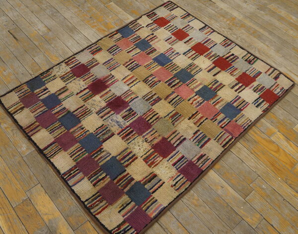 Checkerboard rug featuring textured squares in multicolored stripes, cream, blue, and red on distressed wood flooring.