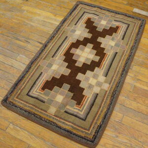 Geometric rug in brown, olive green, gray, and beige squares sits diagonally on rustic hardwood planks.