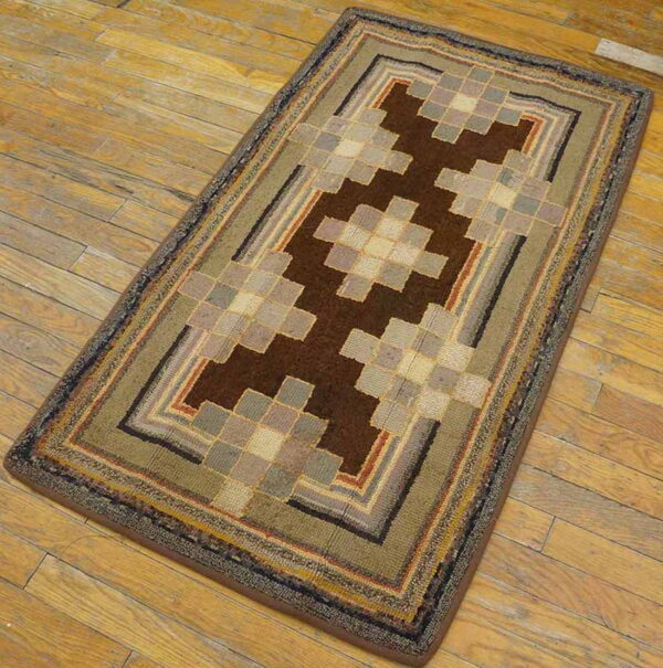 Geometric rug in brown, olive green, gray, and beige squares sits diagonally on rustic hardwood planks.