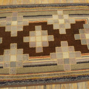 Hooked rug displaying dark brown geometric blocks surrounded by gray, beige, and green borders on wood.