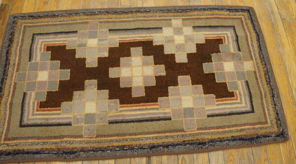 Hooked rug displaying dark brown geometric blocks surrounded by gray, beige, and green borders on wood.