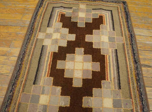 A chunky pile runner rug with a stepped brown and multicolored checkerboard design lies on wood flooring.