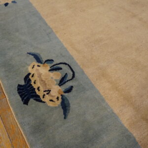 Tan rug with a blue border detailed with cream and navy floral patterns rests on distressed wood.
