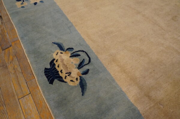 Tan rug with a blue border detailed with cream and navy floral patterns rests on distressed wood.