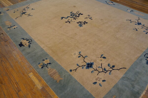 A large tan rug with blue floral branches and a teal border sits on wood flooring.