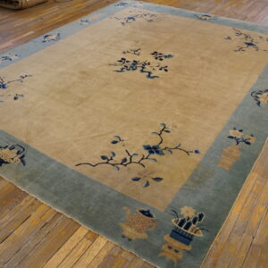 Tan rug with low pile features blue floral sprays and a wide sage border on distressed hardwood floors.