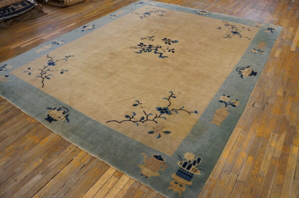 Tan rug with low pile features blue floral sprays and a wide sage border on distressed hardwood floors.