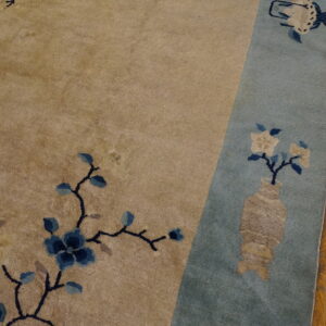 Beige rug field with blue floral vines borders a pale blue section containing a vase motif on wood planks.