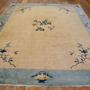 Tan rug with blue floral branches and a wide blue border rests on a distressed wooden floor.