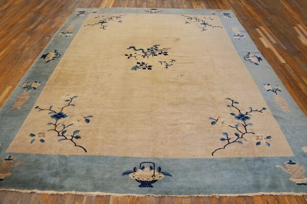 Tan rug with blue floral branches and a wide blue border rests on a distressed wooden floor.