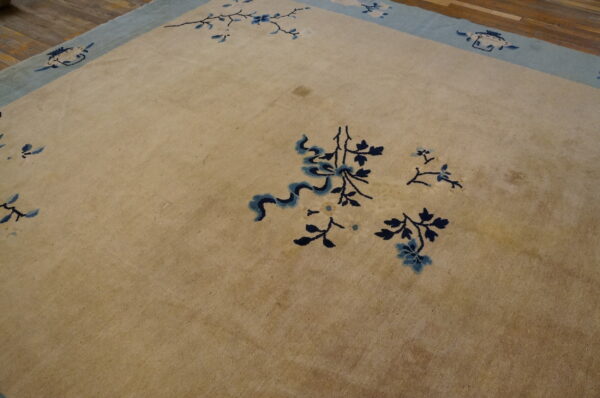 Beige rug featuring scattered blue floral motifs and a light blue border on wood flooring.