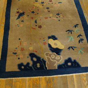 Tan pictorial rug with colorful birds and blossoms, bordered in deep blue, rests on golden wood planks.