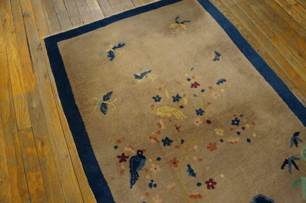 A taupe rug with blue birds and pink flowers rests on wide plank hardwood floors.